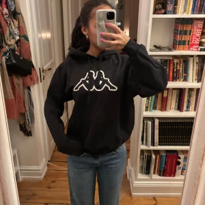 Svart hoodie från Kappa med logga - Svart hoodie från Kappa med stor vit logga på bröstet. Super najs!