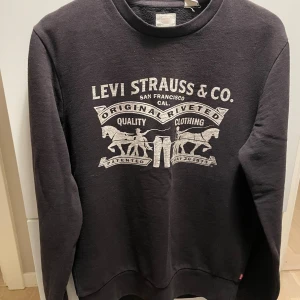 Svart sweatshirt från Levi's - Svart sweatshirt från Levi's med klassiskt tryck framtill i vitt. Tröjan har rund halsringning och långa ärmar. Tillverkad i mjuk bomullsmix som är skön att ha på sig. Perfekt för en avslappnad stil.