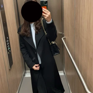 Svart lång kappa med bred krage - Säljer en svart, stilren och lång kappa med bred krage och knappstängning framtill. Perfekt för dig som gillar minimalistisk och klassisk look. Kappan har lång ärm och rak passform, vilket gör den enkel att matcha med olika outfits.