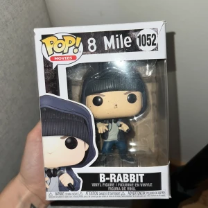 Funko Pop! Movies 8 Mile B-Rabbit #1052 - Säljer en Funko Pop! Movies 8 Mile B-Rabbit #1052. Figuren är i nyskick och levereras i originalförpackning. Notera att kartongen har en tydlig skada i ett hörn (se bild), men figuren är oskadad. Perfekt för samlare av filmrelaterade Funko Pop!