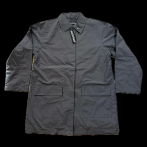 Grå rock från Matterhorn - Snygg grå rock från Matterhorn med klassisk krage och stora framfickor. Jackan har knäppning med knappar och stilren design utan synliga detaljer. Perfekt för dig som gillar minimalistisk och clean look. Materialet är polyester och jackan har långärmade ärmar.