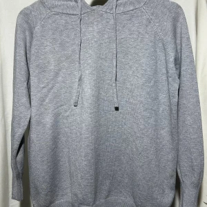 Grå stickad hoodie  - En stilren grå stickad hoodie med huva och snörning. Tröjan har långärmad design och ribbade muddar vid ärmslut och nederkant. Perfekt för en avslappnad och chill look.