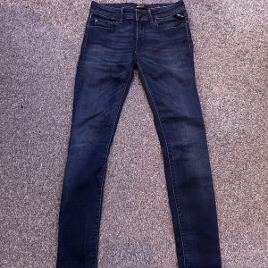Mörkblå jeans från Replay - Snygga mörkblå jeans från Replay med klassisk femficksdesign och diskreta sömmar på bakfickorna. Jeansen har normal passform i midjan och är tillverkade i stretchigt denim för en bekväm känsla. Perfekta till sneakers eller boots.