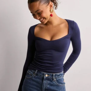 Mörkblå långärmad polotopp - Snygg mörkblå långärmad polotopp med djup v-ringning och diskret spetskant runt halsen. toppen är helt ny och oanvänd samt med prislappen fortfarande på! storlek M