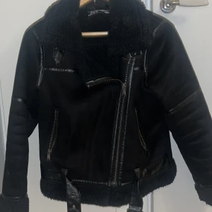 Svart teddyjacka från Zara - Säljer en svart teddyjacka från Zara med coola detaljer i skinnimitation och grov dragkedja. Jackan har en stor krage i teddy, två fickor med dragkedja och bälte nedtill. Perfekt för dig som vill ha en snygg och varm jacka. Storlek XS passar S och M.  Bra skick! Köparen står för frakten (69k)kr