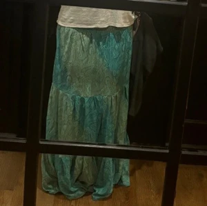 Turkos långkjol med paisleymönster - Säljer en turkos långkjol med paisleyinspirerat mönster och volangdetalj. Kjolen har en luftig och flowy känsla, perfekt för varmare dagar. Den har en mjuk, böljande form och är riktigt skön att bära. Jag är 184 och den går ner i marken för mig men går o lägga upp den ifall man är kortare. Köpte den i en spansk butik i somras och nu inte kommit till min användning. Den är i mycket bra sick då den är använd få gånger. Skriv ifall ni vill ha flera bilder!😽