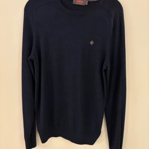 Mörkblå merinoulltröja från Morris - Säljer en stilren mörkblå tröja från Morris i 100% merinoull. Tröjan har rund halsringning, diskret logga på bröstet och långa ärmar. Perfekt för dig som gillar klassisk och enkel stil.