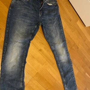 Blå cargopants från SMOG - Säljer ett par blå cargopants från SMOG med slitna detaljer och stora fickor på benen. Byxorna har klassisk jeanslook, raka ben och är tillverkade i bomullsmaterial. Perfekt för dig som gillar streetstyle och funktionella plagg.