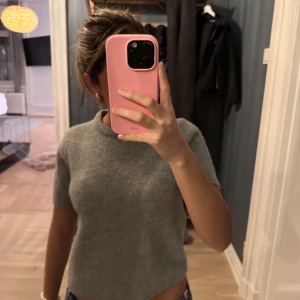 Grå stickad kortärmad tröja från Zara - Mysig grå stickad tröja från Zara med korta ärmar och rund halsringning. Tröjan har en rak, något croppad passform och ribbade kanter vid ärmslut och nederkant. 