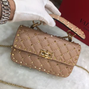 Beige quiltad handväska från Valentino - Säljer en beige handväska från Valentino med quiltad design och guldiga nitar. Väskan har en snygg kedjerem och ett elegant spänne framtill. Perfekt för dig som gillar lyxiga detaljer och vill sticka ut med en ikonisk accessoar(DETTA ÄR EN BESTÄLLNINGSVARA SOM TAR 1-3 VECKOR ATT FÅ HEM)🫰🫰box dustbag osv får du med!