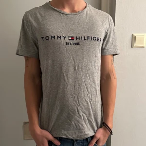 Grå t-shirt Tommy Hilfiger - Tommy Tisha i storlek M i okej skick. Kan behöva en strykning som ni ser på bilderna ;)! Billigt pris tveka inte för o Skrih vid frågor. 180, 65 pannor. Må bäst! 