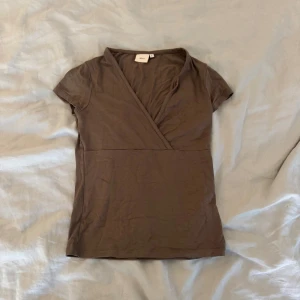 Brun omlottopp  - Säljer en brun omlottopp från Nelly i storlek S. Toppen har korta ärmar, v-ringning och är tillverkad i mjuk bomull. Basic men med detaljer🤎- läs min bio för information 💌