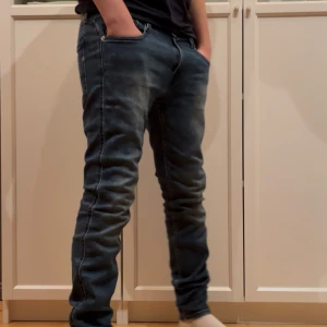 Blå Replay Anbass  - Säljer ett par blå jeans från Replay med snyggt tvättad look och klassiska bakfickor. Jeansen har tapered passform och normal midja, med Replay-logga vid fickan. Perfekta för dig som gillar stilrena och bekväma jeans. Replay Anbass Storlek 30/32.