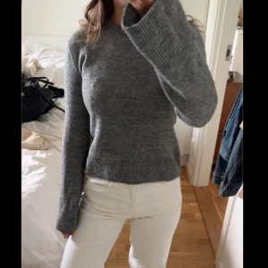 Grå stickad tröja med långa ärmar - Mysig grå stickad tröja med rund hals och långa, något utsvängda ärmar. Tröjan har en enkel och stilren design som är lätt att matcha med olika outfits. Perfekt för kyliga dagar och passar dig som gillar en klassisk look.