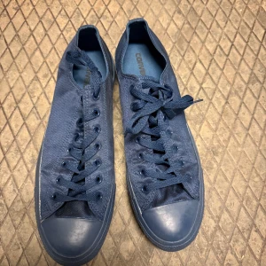 Mörkblå Converse All Star sneakers - Snygga mörkblå Converse All Star sneakers med klassisk låg modell i storlek 46. Skorna har rund tå, platt sula och är tillverkade i slitstark canvas med gummidetaljer på tå och sula. De har snörning och en stilren, monokrom look som passar till det mesta.