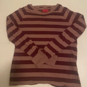 Randig långärmad tröja Hugo Boss - Snygg långärmad tröja från Hugo Boss i storlek S. Tröjan har breda horisontella ränder i mörkbrunt och beige, med ribbad halsringning. Perfekt för dig som gillar klassisk stil med en twist. Materialet är mjukt och känns skönt mot huden.