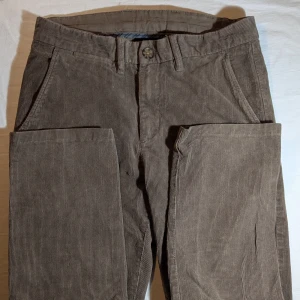 Bruna manchesterbyxor - Stilrena och tidlösa bruna manchesterbyxor i klassisk passform. Perfekta för både vardag och mer dressade tillfällen. Den mjuka manchestern ger en bekväm känsla och exklusiv look som funkar året runt. Har två bakfickor med knapp och fina detaljer som gör dem både praktiska och eleganta. Passar perfekt med en vit skjorta, stickad tröja eller overshirt för en modern vintage-stil.  📏 Storlek: 30W/32L 🎨 Färg: Mjuk brun / taupe 🧶 Material: Manchester / bomull 🧼 Skick: knappt använda