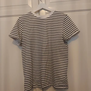 Randig t-shirt från FB Sister - ⚠️ Skriv till mig innan köp!⚠️Snygg vit t-shirt med svarta horisontella ränder från FB Sister. Modellen är regular fit med korta ärmar och rund hals. Perfekt för dig som gillar klassisk och enkel stil. Materialet är mjuk bomull som känns skönt mot huden.