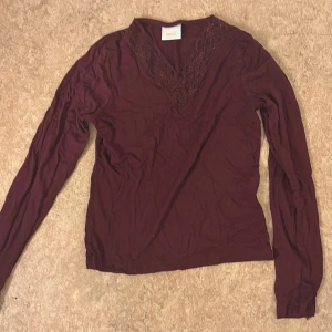 Vinröd långärmad topp från Gina Tricot - Vinröd långärmad topp från Gina Tricot med v-ringning och spetsdetaljer längs halsringningen. Tunn och mjuk i materialet, perfekt för lager-på-lager eller som den är.