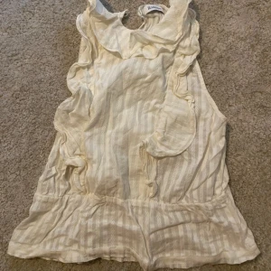 Randig volangblus från Rodebjer - Säljer en ljus, randig blus från Rodebjer med volangdetaljer längs axlar och halsringning. Blusen är ärmlös och har en mjuk, flowy passform som ger en chill vibe. Perfekt för dig som gillar stilrena och romantiska toppar.