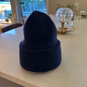 Mörkblå ribbad stickad mössa - KASHMERE MÖSSA! Snygg mörkblå mössa med bred uppvikt kant och ribbad stickning. Perfekt för kalla dagar och enkel att matcha med din jacka eller hoodie. Klassisk form som sitter skönt på huvudet och ger en chill vibe.