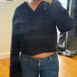 Mörkblå kofta med knappar från Gina Tricot - Säljer en mörkblå, croppad kofta från Gina Tricot med v-ringning och dekorativa knappar framtill. Koftan har lång ärm och är gjord i ett mjukt, lite tjockare material som passar perfekt till lager på lager. Enkel och stilren design som funkar till allt.