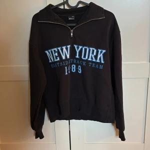 Svart half zip hoodie med New York-tryck - Svart hoodie med halv dragkedja och blått New York-tryck framtill. 