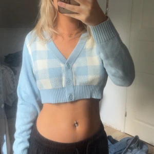 Croppad rutig kofta från Divided XS - Superfin croppad kofta från Divided i ljusblått och vitt med rutigt mönster framtill. Koftan har v-ringning, ribbade muddar och knappar framtill. Perfekt för lager-på-lager och ger en söt och trendig look.