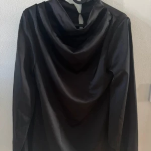 Svart satintopp med draperad hals - Säljer en svart långärmad topp i glansigt satinmaterial med snygg draperad halsringning. Perfekt för dig som gillar en elegant och stilren look. I storlek 36 från Boohoo, aldrig använd.🤍
