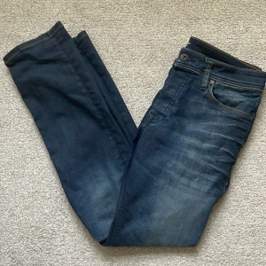 Mörkblå jeans från Jack & Jones - Snygga mörkblå jeans från Jack & Jones med klassisk femficksdesign och kontrastsömmar. Jeansen har en slim/straight passform och är tillverkade i slitstarkt denimtyg. Läderpatch med logga baktill i midjan ger en schysst detalj. Perfekta till en avslappnad stil. L:29 W:30