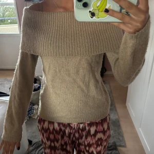 Beige offshoulder stickad tröja Stories - Superfin beige stickad tröja från & Other Stories med bred ribbad offshoulder-krage. Långärmad och mjuk, perfekt för lager på lager under höst och vinter. Snygg passform som sitter lite tightare över kroppen.