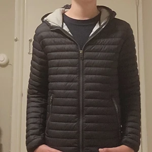 Svart dunjacka från Colmar med huva - Säljer en svart dunjacka från Colmar med huva och ljusgrått foder. Jackan har quiltad design, dragkedja framtill och två fickor med dragkedja. Perfekt för kyliga dagar och är riktigt snygg.