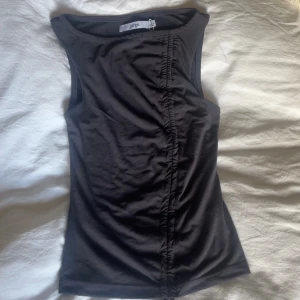 Svart linnetopp med snörning från Jorge - Säljer en svart ärmlös linnetopp från Jorge med snygg snörningsdetalj framtill som ger en rynkad effekt. Toppen har rund halsringning och är tillverkad i ett mjukt, stretchigt material som sitter tight mot kroppen. Perfekt att styla med jeans eller kjol.