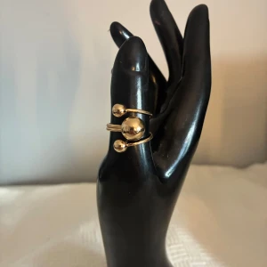 Guldfärgad ring men kulor - Cool guldfärgad ring med tre glänsande kulor i olika storlekar. Ringen har en modern och unik design med öppet band som ger en edgy vibe. Perfekt för dig som vill sticka ut med ditt smycke och addera lite bling till din look.