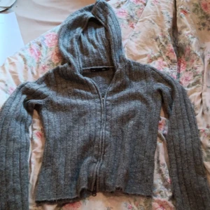 Grå ribbad hoodie från 157 - Mysig grå hoodie från 157 i ribbstickat material. Tröjan har huva, dragkedja framtill och långa ärmar. Perfekt för lager-på-lager och chill dagar. Enkel och stilren design som funkar till det mesta.