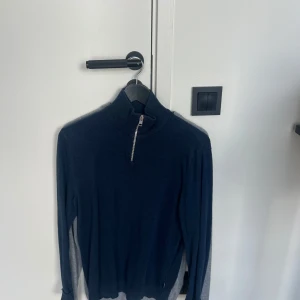 Mörkblå stickad tröja med half zip - Mörkblå stickad tröja med hög krage och half zip-dragkedja framtill. Tröjan har långärmad.. Jack and Jones storlek S passar M. 