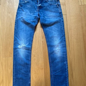 Blå Dondup jeans, stl 31 - Säljer ett par blå jeans från Dondup, modell SAM, i storlek 31. Jeansen har slitna detaljer på både fram- och baksida, klassisk femficksdesign och smal passform. Tillverkade i bomull med snygg tvätt och lätt slitning för en cool look.