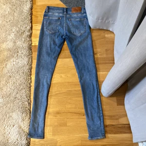 Blå jeans från Tiger of Sweden - Säljer ett par klassiska blå skinny jeans från Tiger of Sweden. Jeansen har fem fickor, normalhög midja och är tillverkade i stretchigt denim för en tight passform. Perfekta för dig som gillar en smal siluett och enkel stil.