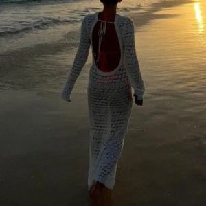 Vit lång stickad strandklänning - Säljer en vit lång stickad klänning med snyggt hålmönster och öppen rygg. Klänningen har lång ärm och är perfekt att dra över bikinin på stranden. Den är figurnära och har en cool boho-vibe med transparent känsla.