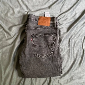 Grå Levi's 511 jeans straight fit - Säljer ett par grå Levi's 511 jeans med klassisk femficksdesign och läderpatch bak i midjan. Jeansen har en rak passform och är tillverkade i slitstarkt denimtyg. Perfekta för dig som gillar en clean och tidlös look.