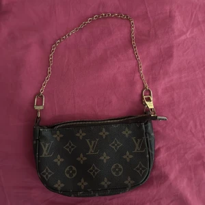 Finaste  axelväska - Snygg liten axelväska  med klassiskt monogrammönster i brunt och beige. Väskan har guldfärgad kedja och dragkedja upptill. Perfekt storlek för det viktigaste och ger en lyxig touch till din outfit.