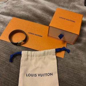 Louis Vuitton armband - Snyggt armband från Louis Vuitton i klassiskt brunt monogrammönster med guldfärgat spänne. Armbandet är gjort i präglat skinn och har märkets ikoniska LV-logga och detaljer. Kommer med originalask, kvitto och dustbag.