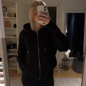 Svart hoodie med dragkedja - Svart hoodie med dragkedja framtill och huva med snören. Klassisk modell med kängurufickor och lång ärm. Perfekt för chill dagar eller när du vill ha en enkel och stilren look.