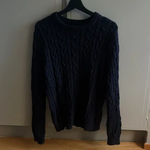 Mörkblå kabelstickad tröja - Säljer en mörkblå kabelstickad tröja med rund hals och långa ärmar. Tröjan har ett klassiskt flätmönster och är perfekt för kyliga dagar. Den är mjuk och skön, passar dig som gillar en enkel men snygg stil.