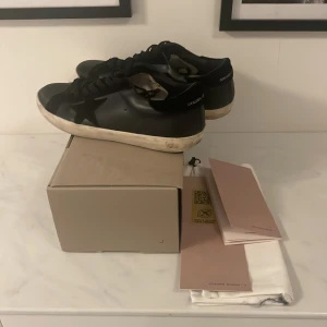 Svarta Golden Goose sneakers - Snygga svarta sneakers från Golden Goose medel klassisk stjärndetalj på sidan. Använda men i mycket nra skick. Finns även ett litet hål där bak men man ser inte den så mycket (sista bilden)