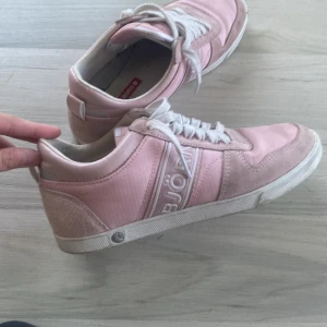 Rosa sneakers från Björn Borg - Snygga rosa sneakers från Björn Borg med vita snören och detaljer i mocka och textil. Skorna har en klassisk låg profil, rund tå och vit sula. 