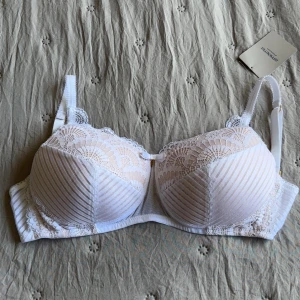 Oanvänd Vit spets-bh Karolina från Amoena - Säljer en snygg vit bh från Amoena, modell Karolina. Bh:n har vackra spetsdetaljer och diskreta ränder på kuporna, samt en liten rosett framtill. Justerbara axelband och hakknäppning bak. Skulle säga den är en storlek mindre i kupan🫶🏻