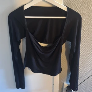 Svart långärmad topp från Gina Tricot - Svart långärmad topp från Gina Tricot med snygg draperad detalj framtill och öppen rygg. Toppen har en tight passform och är tillverkad i mjuk, stretchig polyester. Perfekt för dig som vill ha en stilren men ändå unik look.