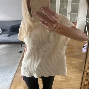 Beige stickad ärmlös topp - Säljer en beige stickad topp med lös passform och korta ärmar. Toppen har en ribbad struktur och är tillverkad i ett mjukt material som ger en avslappnad vibe. Perfekt att styla med jeans eller kjol för en enkel och snygg look.
