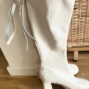 Beige/rosa höga stövlar med klack - Snygga beige/rosa stövlar i skinnimitation med hög klack och rund tå. Stövlarna har dragkedja på baksidan. Dom går strax under knät och har en V-skärning. Dom är använda och lite repiga vid tån men i övrigt är dom rena och hela.                                                     (Läs alltid min profil för villkor)